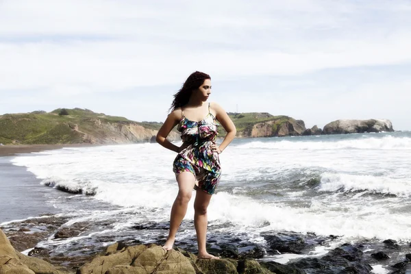 Latina Frau steht in Kleid auf Felsen am Strand — Stockfoto