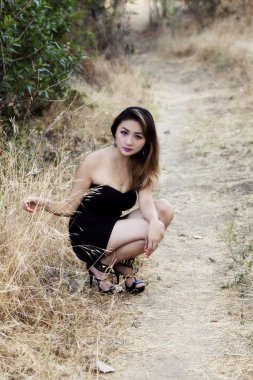 Toprak yol boyunca çömelme çekici Asyalı Amerikalı siyah elbise