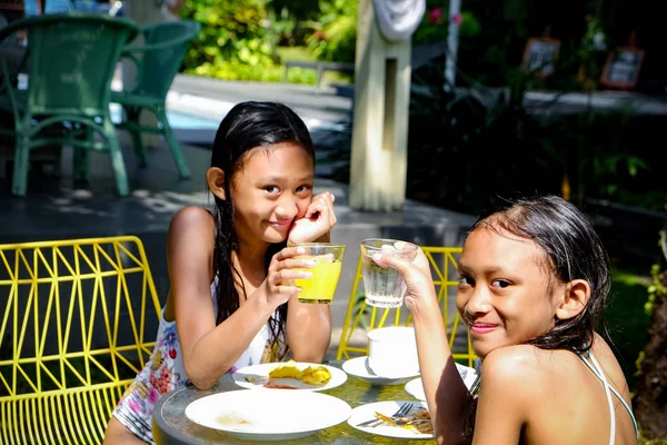 Két ázsiai lány fürdőruhában eszik valamit úszás után. Pohárköszöntőt mondok. Néző és mosolygó — Stock Fotó