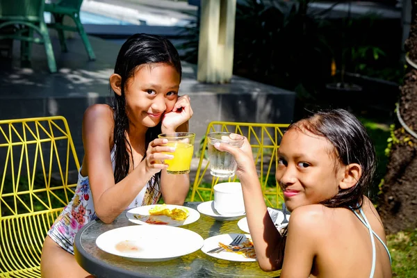 Dos chicas asiáticas en traje de baño comiendo algunas comidas después de nadar actividades. Hacer un brindis. Mirando y sonriendo —  Fotos de Stock
