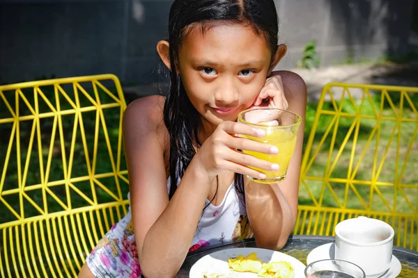 Ritratto di ragazza adolescente asiatica carina in costume da bagno con un bicchiere di succo d'arancia sano sulle mani, mentre mangia dopo aver nuotato — Foto Stock