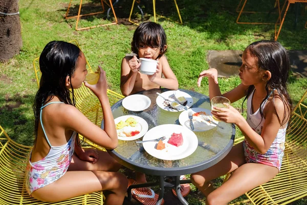Mayo giymiş neşeli Asyalı çocuklar yüzme etkinliklerinden sonra birlikte yemek yiyip eğleniyorlar. — Stok fotoğraf
