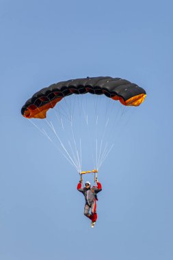 Paraşütçü mavi gökyüzüne kırmızı bir paraşütle iniyor.