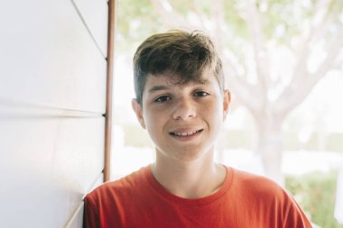 Kameraya bakarken tahta duvara yaslanan neşeli bir gencin portresi.