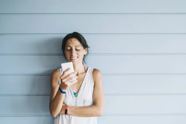 Hermosa mujer adulta apoyada en una pared de madera mientras usa un teléfono inteligente — Foto de Stock