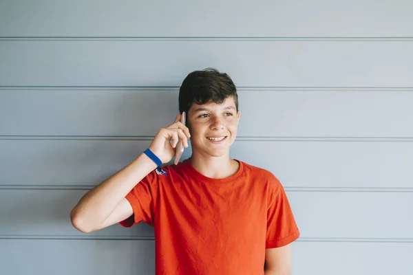 Jeune adolescent avec t-shirt rouge debout contre le mur tout en utilisant le téléphone — Photo
