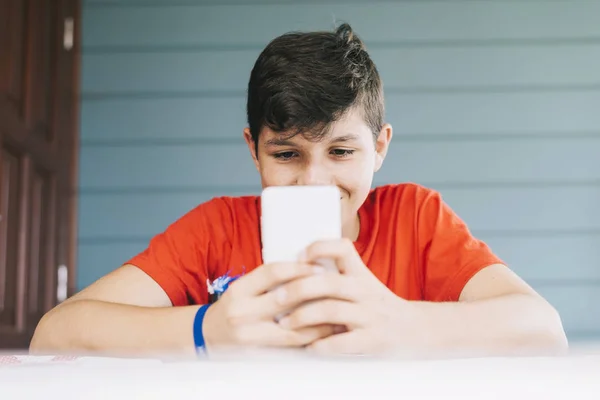 Bonito caucasiano de 13 anos de idade menino vestindo camiseta vermelha sentado ao ar livre usando gadget eletrônico — Fotografia de Stock