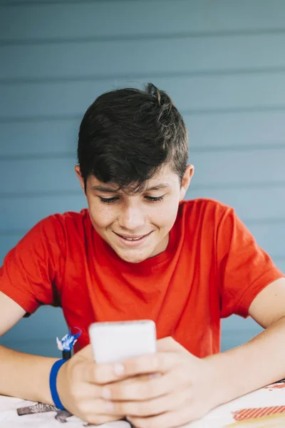 Bonito caucasiano de 13 anos de idade menino vestindo camiseta vermelha sentado ao ar livre usando gadget eletrônico — Fotografia de Stock