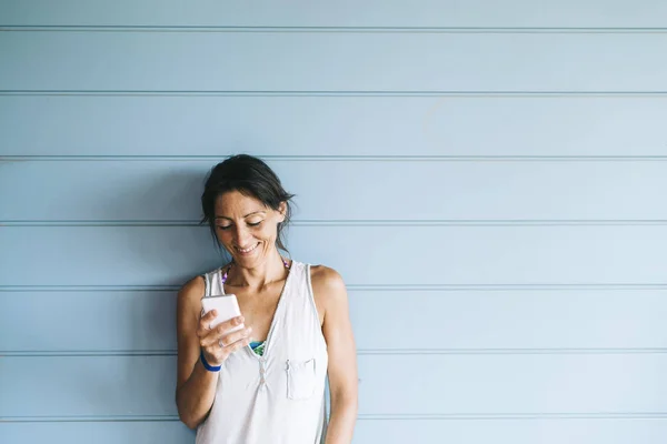 Hermosa mujer adulta apoyada en una pared de madera mientras usa un teléfono inteligente — Foto de Stock