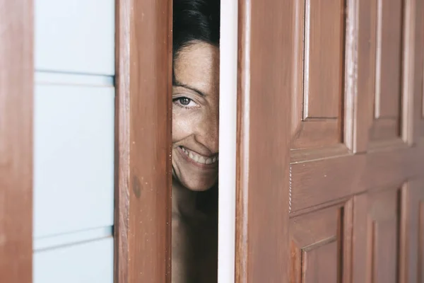 Femme souriante regardant entre porte ouverte et mur — Photo