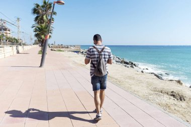 Güneşli bir günde, sırt çantalı bir adamın deniz kıyısında gezinti yaptığını gördüm.