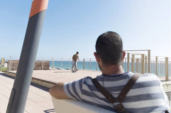 Vista trasera de un hombre sentado en el paseo marítimo mirando al horizonte — Foto de Stock