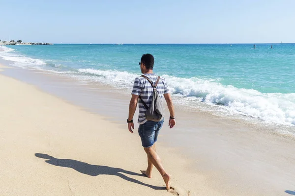 Vista trasera de un hombre con mochila alejándose en la orilla del mar en un día soleado —  Fotos de Stock