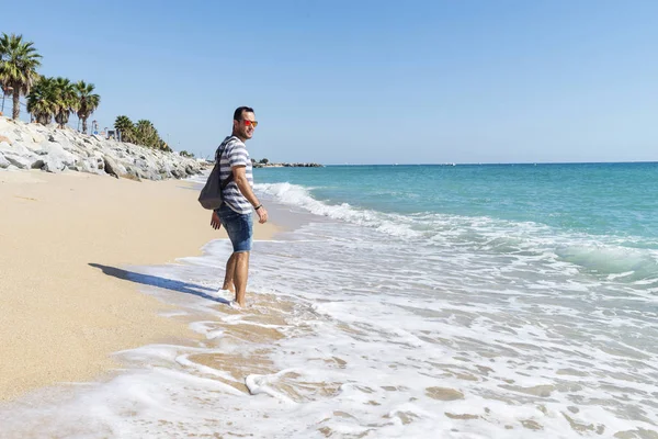 Vista trasera de un hombre con mochila alejándose en la orilla del mar en un día soleado — Foto de Stock