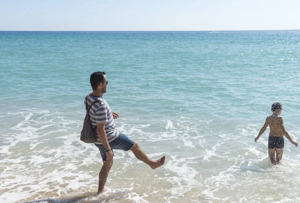 Батько і син грають з водою на березі моря в сонячний день — стокове фото