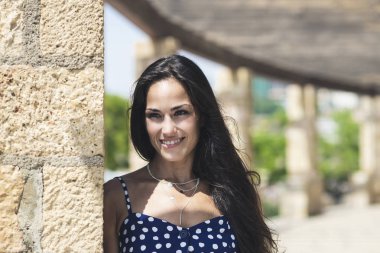 Güzel, mavi elbiseli İspanyol kadın. Duvara yaslanmış, başka tarafa bakıyor.