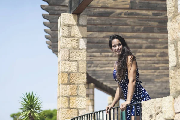 Gyönyörű spanyol nő kék ruhában, a kerítésre támaszkodik, miközben félrenéz. — Stock Fotó