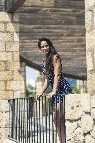 Mulher hispânica bonita em vestido azul apoiando-se na cerca enquanto olha para longe — Fotografia de Stock