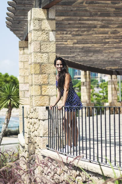 Mulher hispânica bonita em vestido azul apoiando-se na cerca enquanto olha para longe — Fotografia de Stock