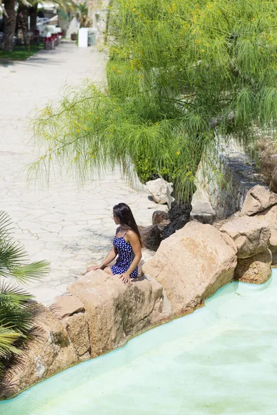A kilátás felett egy csinos fiatal spanyol nő ül a sziklán, egy tó mellett. — Stock Fotó