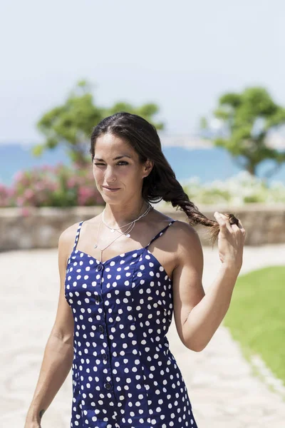 Hermosa mujer hispana en vestido azul de pie contra el mar mientras toca el cabello —  Fotos de Stock