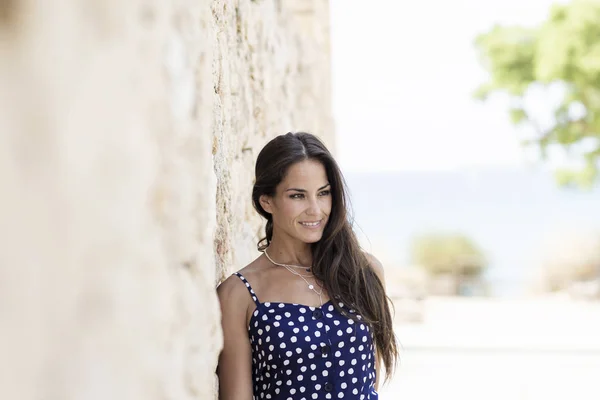 Gyönyörű spanyol nő kék ruhában, a falra támaszkodik, miközben félrenéz. — Stock Fotó