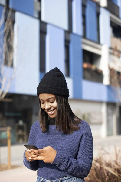 Portrait of African American young beautiful woman wearing a wool cap standing on the street while using a mobile phone — 스톡 사진