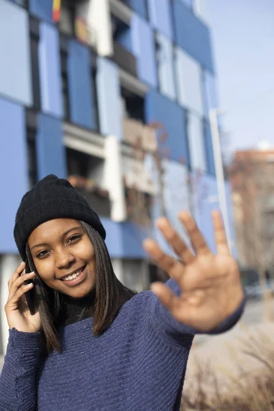 Portrait of African American young beautiful woman wearing a wool cap standing on the street while using a mobile phone — 스톡 사진