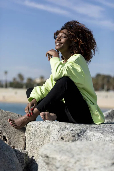 Όμορφη Αφρο-Αμερικανίδα που κάθεται στην ακτή σε μια ηλιόλουστη μέρα — Φωτογραφία Αρχείου