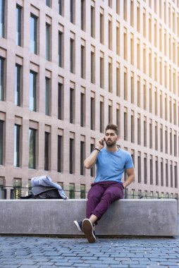 Neşeli modern iş adamının portresi telefonla konuşuyor ve dışarıda bankta otururken gülümsüyor.