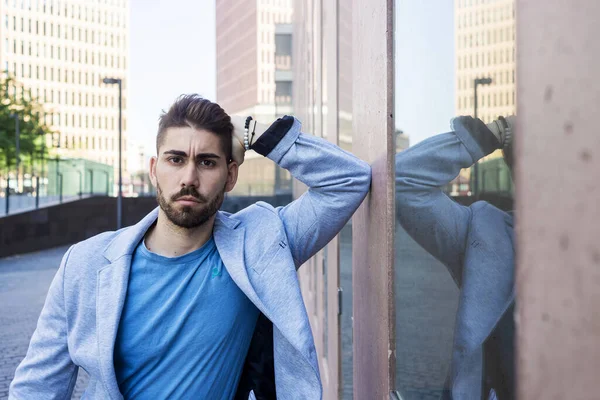 Young bearded man, model of fashion, in urban background wearing casual clothes while leaning in a wall