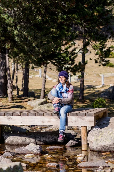 Frau Mit Wollmütze Sitzt Auf Einer Holzbrücke Über Einen Bach — Stockfoto