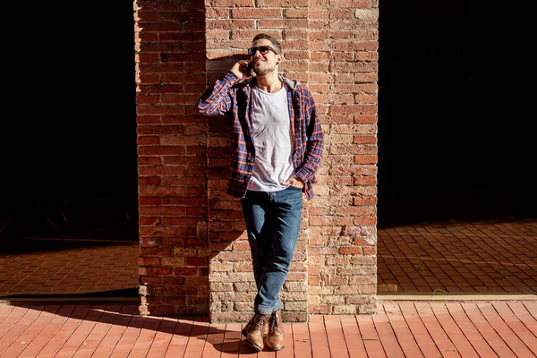 Young Bearded Male Leaning Bricked Wall Wearing Sunglasses While Using — Stock Photo, Image