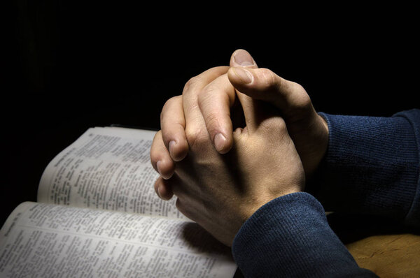 Hands folded in prayer over Scriptures