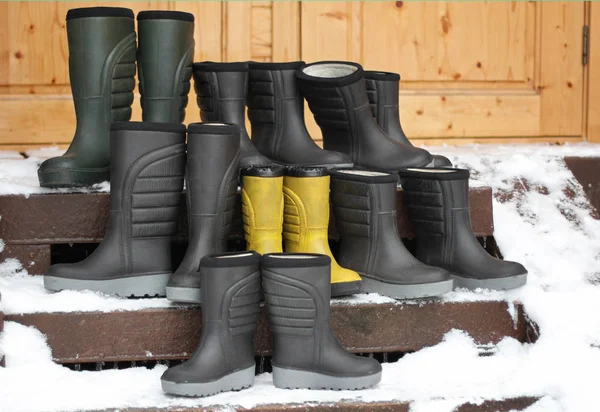 Group of winter polyurethane  boots different sizes and colors standing on wooden porch. Seasonal shoes for all family, adult and child footwear. — Stock Photo, Image