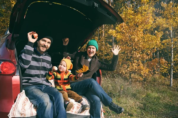 Família feliz descansando após o dia passando ao ar livre no parque de outono. Pai, mãe e filho sentados dentro do porta-malas do carro, sorrindo e olhando para a câmera. Viajar na época de outono . — Fotografia de Stock