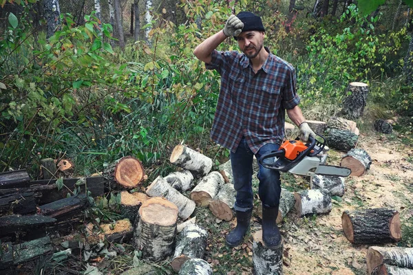 Tired woodcutter after hard work in forest with chainsaw. lumberjack saws a fallen birch tree.