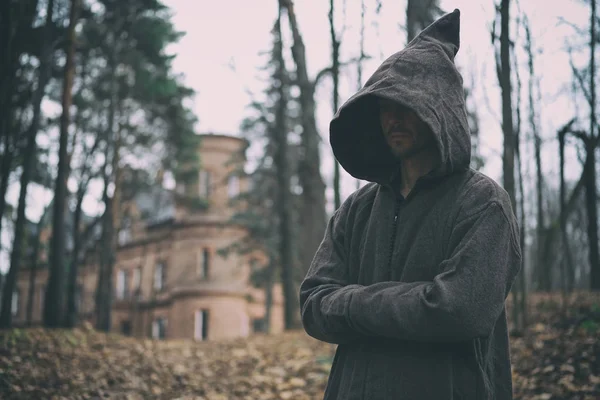 Misterioso monje o mago con bata encapuchada se levanta en el bosque contra el fondo del castillo o monasterio medieval . — Foto de Stock