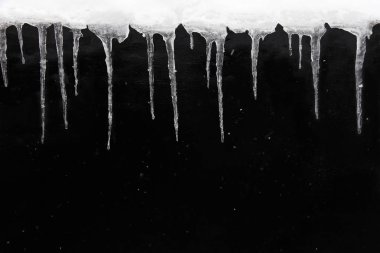 Kış ya da bahar dönemi konsepti. Islak, siyah desenli duvarda buz saçakları ve yağan karlar. Boşluğu kopyala. 