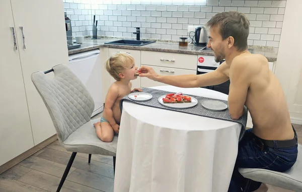 Vader geeft zijn zoontje ontbijt in de keuken. Familie 's morgens thuis. Authentiek lifestyle imago. Brunch met gezonde groentesandwich. — Stockfoto