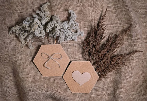 Lasting faded sustainable flowers with two hexagonal frame and cardboard heart on natural canvas background. Composition of dried flowers for Valentine's day on natural earth tone color burlap. — Stock Photo, Image