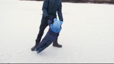 Babası ve küçük çocuğu donmuş gölde eğlenirken gülüyorlar. Baba çocuğunun ellerini tutup etrafında döndürüyor. Aile kış tatillerinde eğleniyor.. 