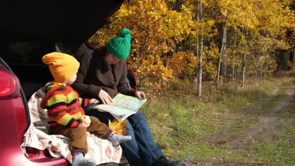 家庭户外野餐 秋天的公路旅行 母亲和他的小孩坐在汽车行李箱里 看着路线图 秋天的旅行 — 图库视频影像