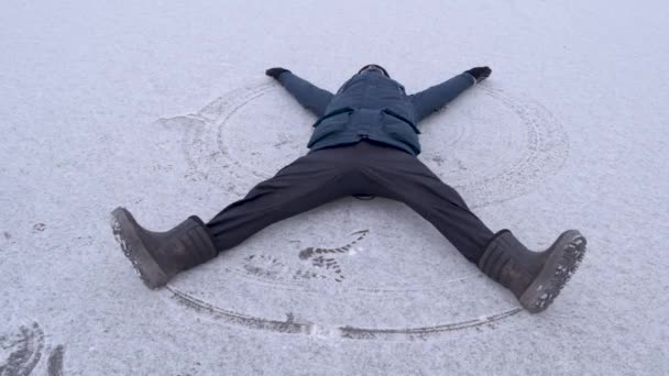 身穿蓝色夹克的成年人躺在结冰的湖面上做雪天使 有趣的家伙寒假快乐 — 图库视频影像