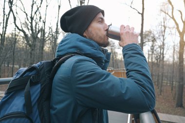 Hipster sakallı bin yıllık klasik mavi ceketli, sonbahar ya da kış parkında yürürken tekrar kullanılabilen paslanmaz şişeden su içen adam. Sıfır atık, sürdürülebilir yaşam. 