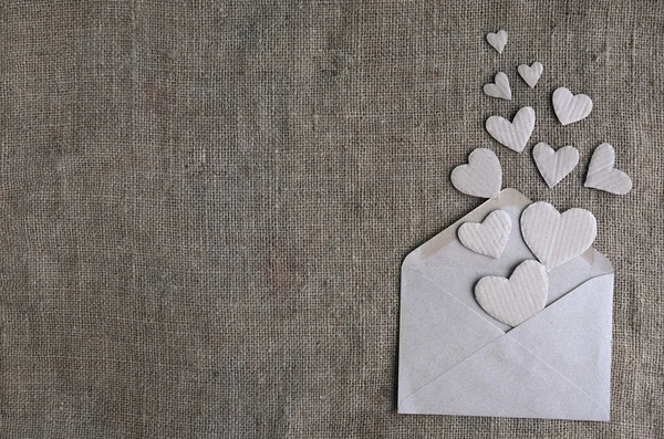 Valentijnskaart in natuurlijke aardetoon kleuren met kopieerruimte. Ambachtelijke papieren envelop met kartonnen handgemaakte hartjes op canvas jute achtergrond. Valentijnsdag, vrouwendag, liefdesverklaring. — Stockfoto