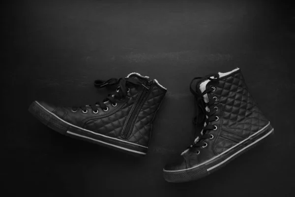 Trendy black quilted sneakers walking on blackboard background. Minimalist black, dark mode, fasion shoes concept. Flat lay, copy space.