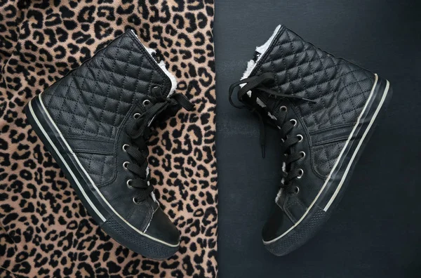 Trendy black quilted leather sneakers on two contrast backgrounds. Animal print and minimalist black. Black and gold cheetah leopard spots textured fabric. Fashion shoes footwear concept. Flatlay.