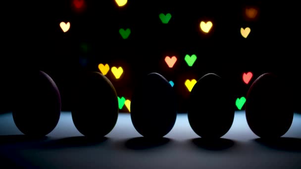 Happy easter concept. Spotlight dancing on row of bright colored eggs on black background with colorful heart shaped lights.