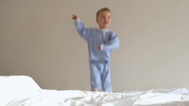 Sabahları mavi çizgili pijamalı, yatakta zıplayan oyuncu bir çocuk. Sevimli anaokulu çocuğu evde eğleniyor. Çocukluk konsepti. Düşük açı.  